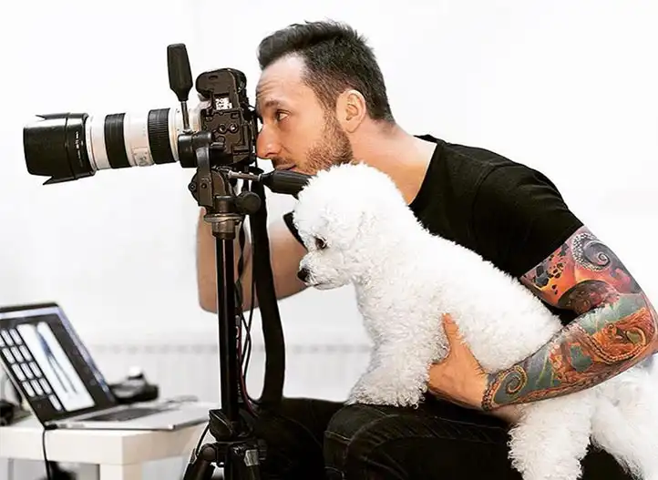 Fotograf przy pracy z aparatem i komputerem, z białym psem na kolanach – fotografia reklamowa i wizerunkowa w Opolu i Wrocławiu