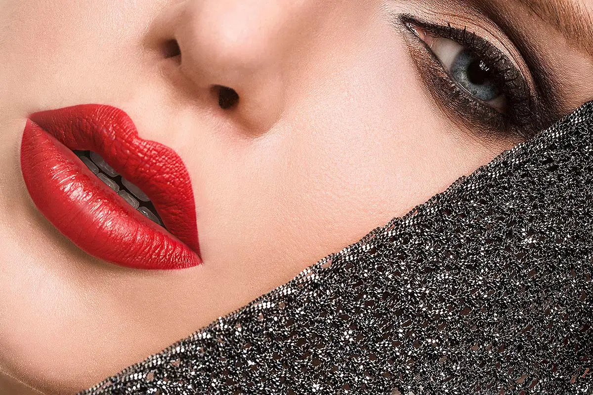 Zbliżenie kobiecej twarzy z czerwonymi ustami i wyrazistym makijażem w sesji reklamowej ręcznie tkanej biżuterii